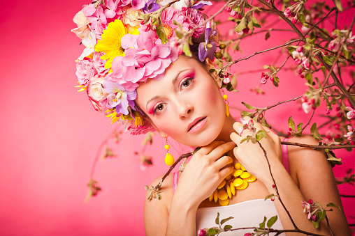 Young lady on a pink background with flower crown under blooming apple tree