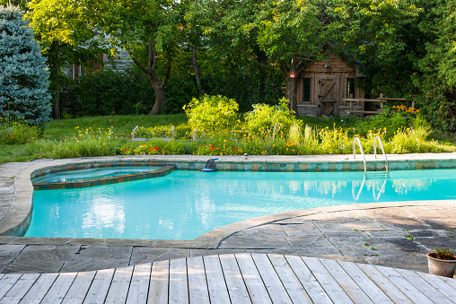 Backyard with outdoor inground residential swimming pool, garden, deck and stone patio