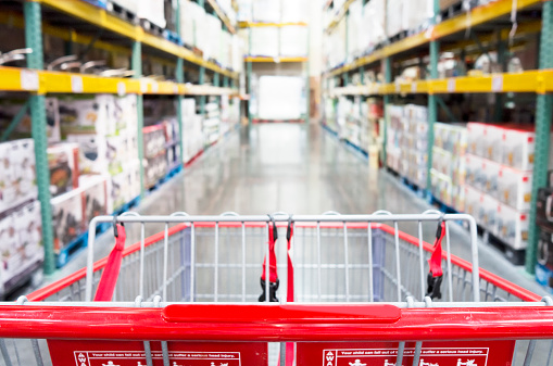 Interior warehouse super store with focus on empty shopping cart in store aisle.