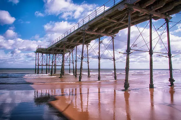 A photograph of Saltburn pier taken from below the walkway as the tide went out, blue skies, fluffy clouds on a bright day with good weather