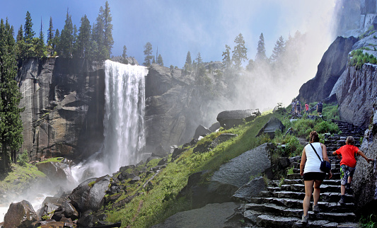 Yosemite, USA - July 26, 2011: two girls climbing stairs towards Vernal falls creating the mist to which the trail has been named: the mist trail. In the background more people are climbing higher up.