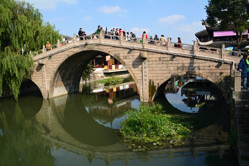 Tourists sightseeing the old Puhui river Bridge in Qibao, an old water town in Shanghai - China.