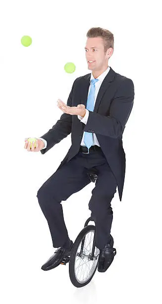 Happy Businessman Juggling Ball Sitting On Unicycle