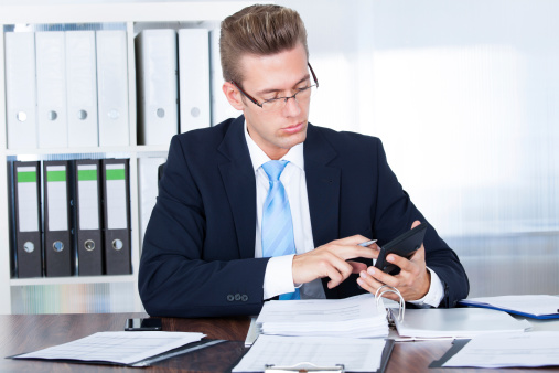 Portrait Of Young Businessman Using Calculator In Office