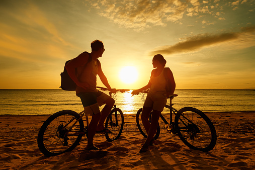 Couple tourists with Bicycles Watching Sunset. Summer Nature Background with Beautiful Sky and Sea. Active Leisure Concept.