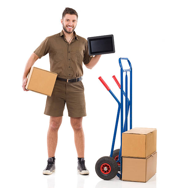 Courier holding a digital tablet Smiling delivery man standing with package under his arm and showing a digital tablet. Full length studio shot isolated on white. mover delivery person box hand truck stock pictures, royalty-free photos & images