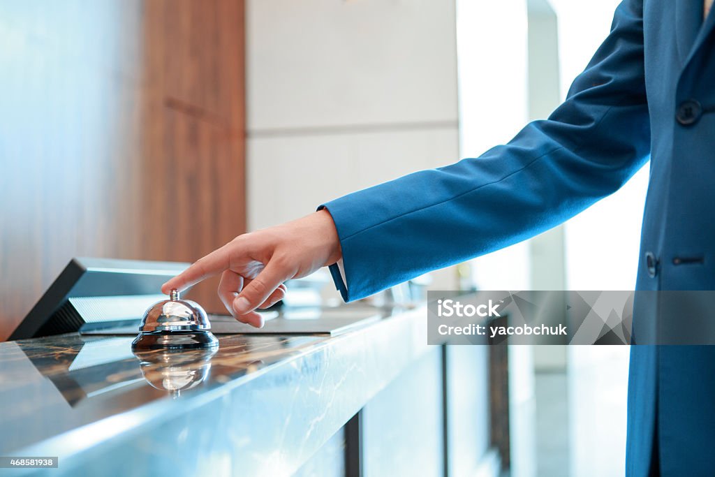 Hotel service bell at reception Service, please. Closeup of a businessman hand ringing silver service bell on hotel reception desk Hotel Stock Photo