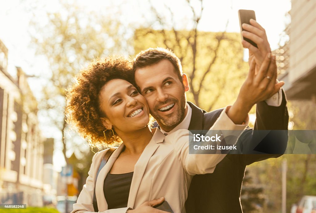 Happy elegance adult couple talking selfie outdoor Cheerful adul couple - afro amercian woman and caucasian man embracing and taking selfie using smart phone outdoor at sunset. Close up of faces. 2015 Stock Photo