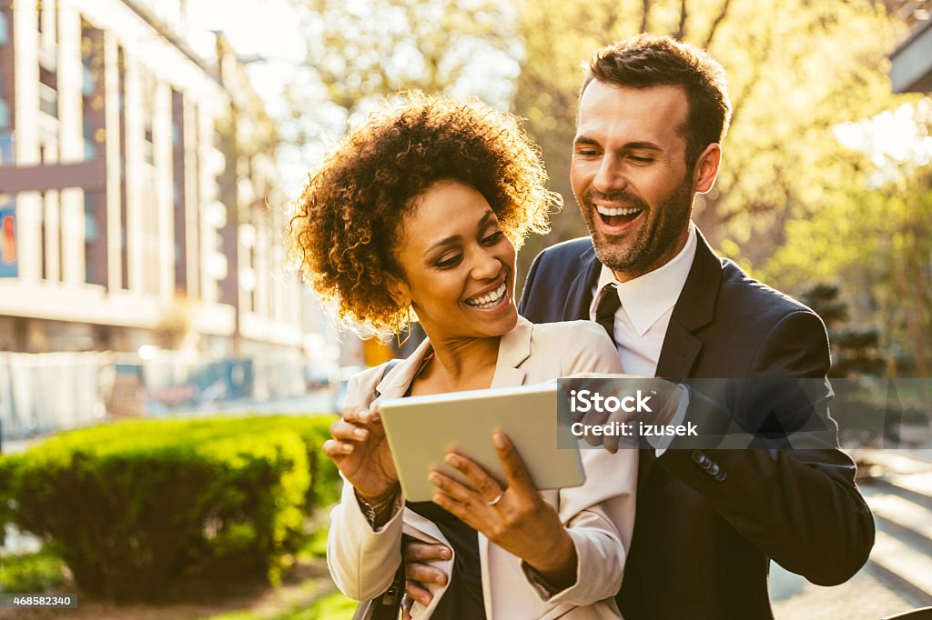Two business people using digital tablet together outdoor Portrait of cheerful caucasian businessman and afro american businesswoman in formal outfits using a digital tablet together outdoor at sunset.  Business Stock Photo