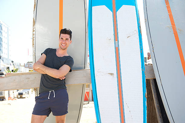 istock Young man smiling and standing with surfboard at the beach 468583303