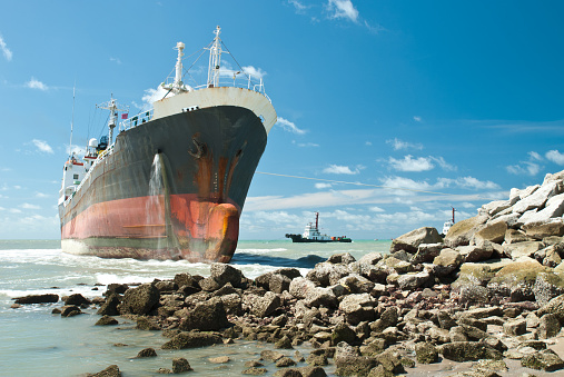 Cargo ship run aground on rocky shore waiting for rescue