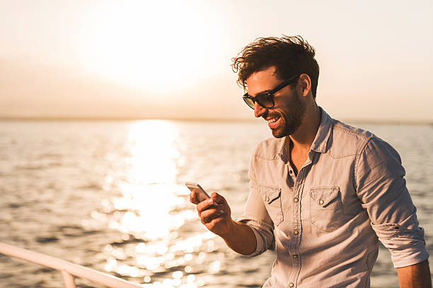 istock Young man using smart phone on a boat at sunset. 468590830
