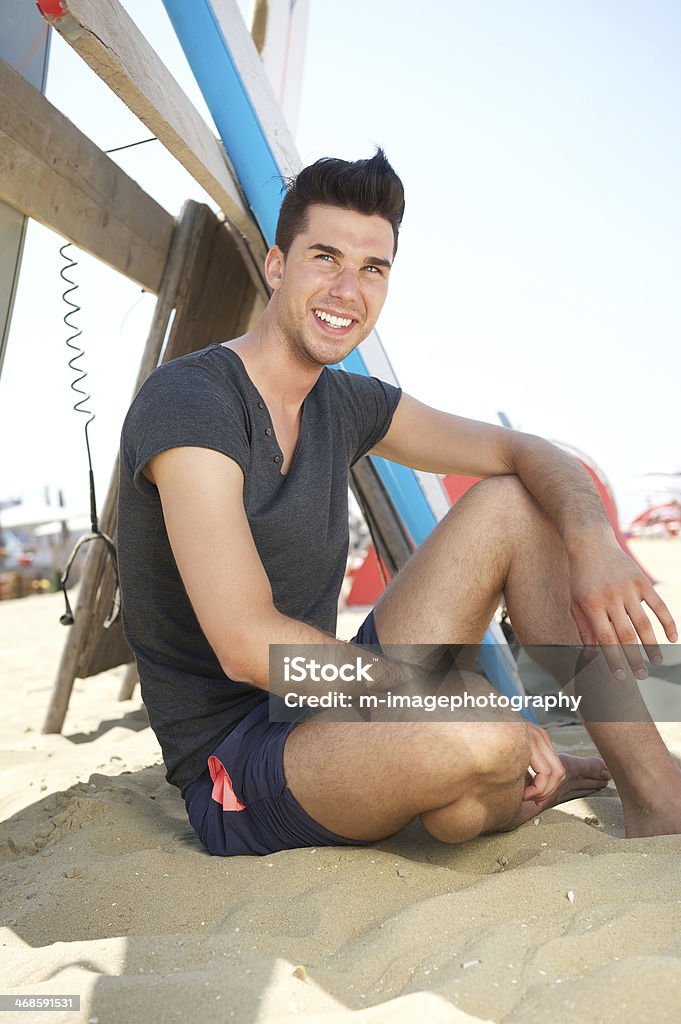 Feliz joven sentado en la playa con olas de planchar - Foto de stock de 20 a 29 años libre de derechos