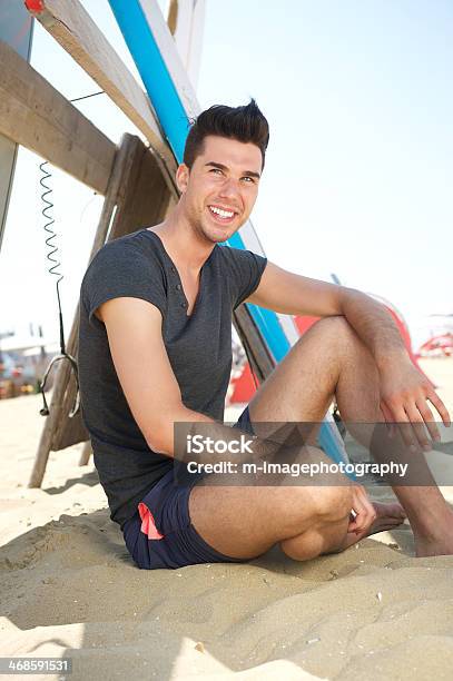 Feliz Joven Sentado En La Playa Con Olas De Planchar Foto de stock y más banco de imágenes de 20 a 29 años