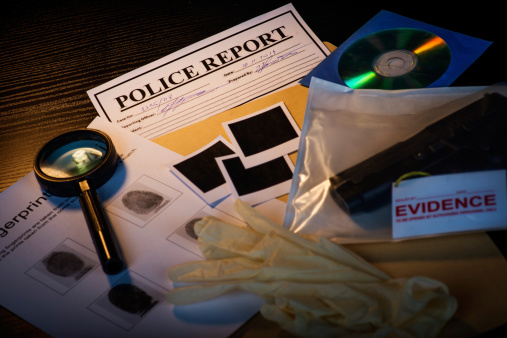 Fictious police desk with crime case records containing gun, blank photos, crime scene information sheet, cd rom, magnifying glass, gloves and police reports.
