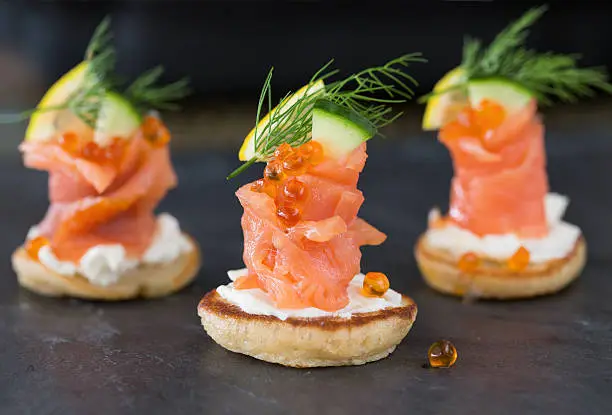 Blini with smoked salmon and sour cream, garnished with dill. Close-up view on dark background