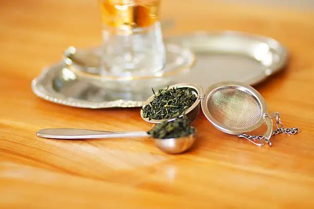 Green tea in spoon on wooden table, in background is a tray with tea glass