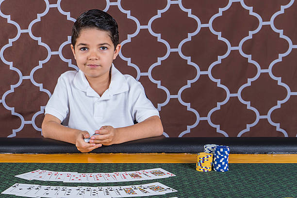 Young boy playing poker at a table A young boy sitting at a poker table gambling playing cards with a brown background child gambling chip gambling poker stock pictures, royalty-free photos & images