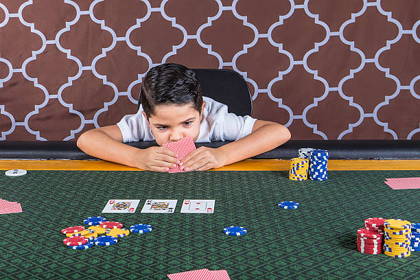 Young boy playing poker at a table A young boy sitting at a poker table gambling playing cards with a brown background child gambling chip gambling poker stock pictures, royalty-free photos & images