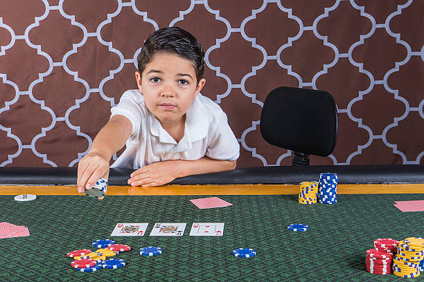 Young boy playing poker at a table A young boy sitting at a poker table gambling playing cards with a brown background child gambling chip gambling poker stock pictures, royalty-free photos & images
