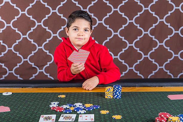 Young boy playing poker at a table A young boy sitting at a poker table gambling playing cards with a brown background child gambling chip gambling poker stock pictures, royalty-free photos & images