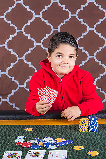 Young boy playing poker at a table A young boy sitting at a poker table gambling playing cards with a brown background child gambling chip gambling poker stock pictures, royalty-free photos & images