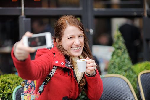 Young woman taking selfie with smart phone in street cafe