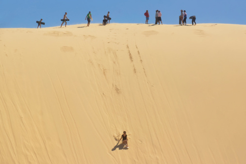 Anna Bay, Australia - January 15, 2014: A woman sandboards down a large sand dune before other tourists at Stockton Beach.