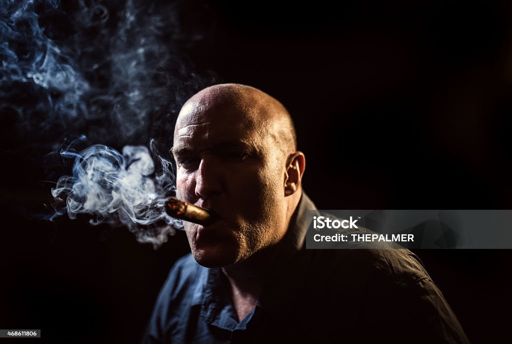 Sinister man smoking a cigar Sinister man smoking a cigar in the dark 2015 Stock Photo