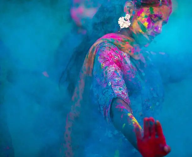 Young woman dancing around blue powder while celebrating the Indian Holi Day