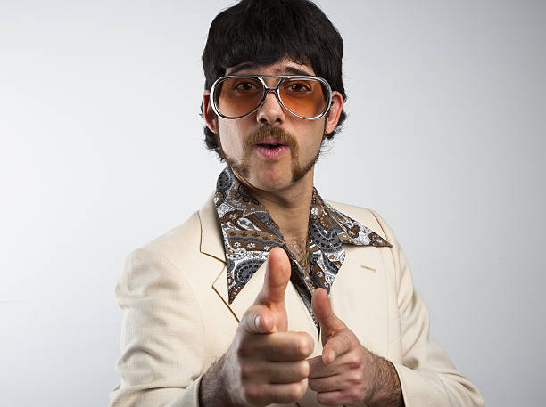 A man dressed in clothes from the '70s on a white background Portrait of a retro man in a 1970s leisure suit and sunglasses pointing to the camera kitsch stock pictures, royalty-free photos & images