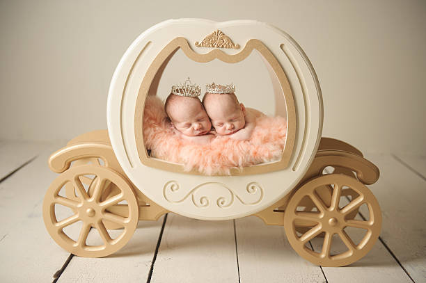 Newborn twin girls sleeping in a princess carriage.
