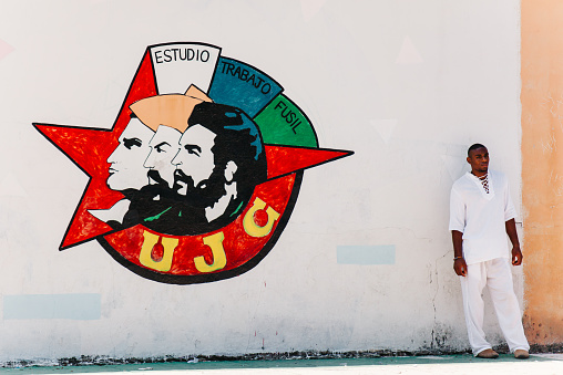 Havana, Cuba - September 5, 2014: A man wearing all white stands by a political wall painting in the streets of Havana, Cuba