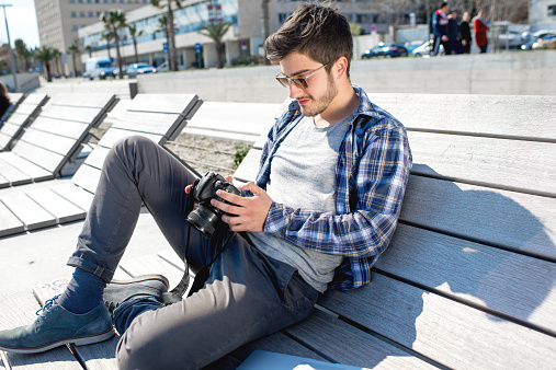 Young photographer holding camera while sitting with laptop on the sunbed