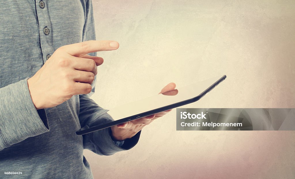 Young man using a tablet computer Young man holding a tablet computer on muted pastel background 2015 Stock Photo