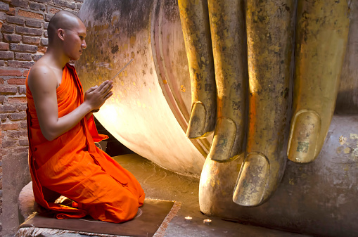 Buddhist monks praying to Lord Buddha with incense at Wat Srichum SuKhothai, Thailand.