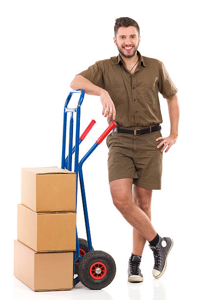 Relexed messenger Cheerful delivery man standing relaxed with a push cart. Full length studio shot isolated on white. mover delivery person box hand truck stock pictures, royalty-free photos & images