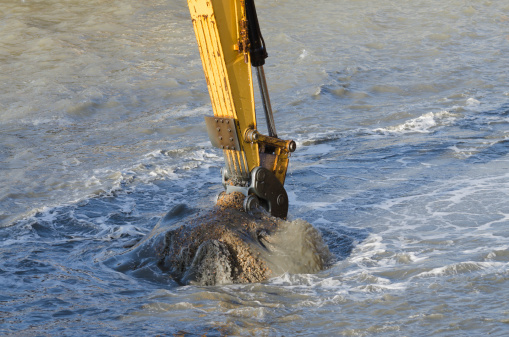 Excavator bucket dredging sand and gravel from the seafront