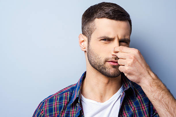 Disgusting smell. Portrait of frustrated young man in casual shirt holding nose and expressing negativity while standing against grey background holding nose stock pictures, royalty-free photos & images