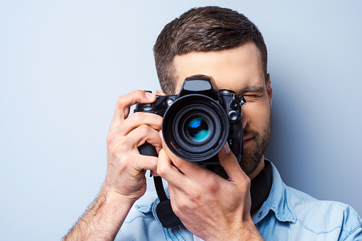 Handsome young man photographing you while standing against grey background