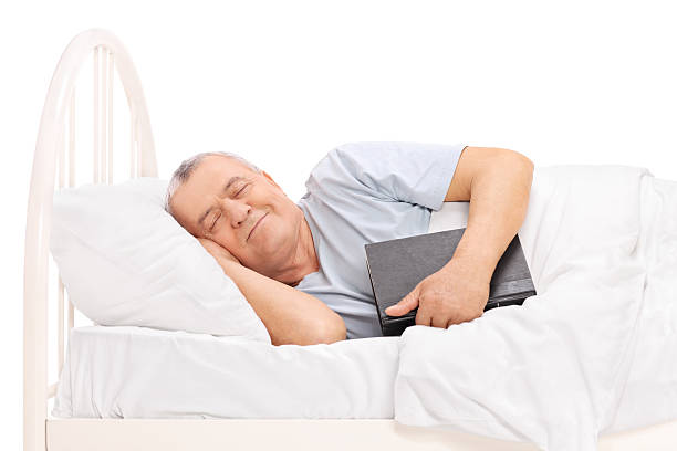 Senior sleeping in a bed and holding a book Senior sleeping in a bed covered with a blanket and holding a book isolated on white background The Best Sleeping Positions for Lower Back Pain: A Complete Guide in 60 year old Soldier Position  stock pictures, royalty-free photos & images