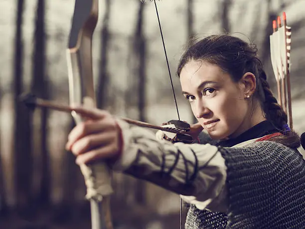 Medieval archer woman, she wearing a chainmail and use a bow and arrow, gloomy forest, cross-processed image.