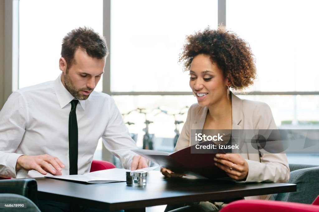 Two business people at lunch in restaurant Afro american businesswoman and caucasian businessman having lunch in restaurant, sitting at the table and reading menu. African Ethnicity Stock Photo
