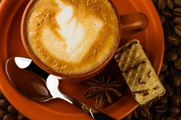 ceramic cup of cappuccino, milk-chocolate wafer and coffee beans on wooden background