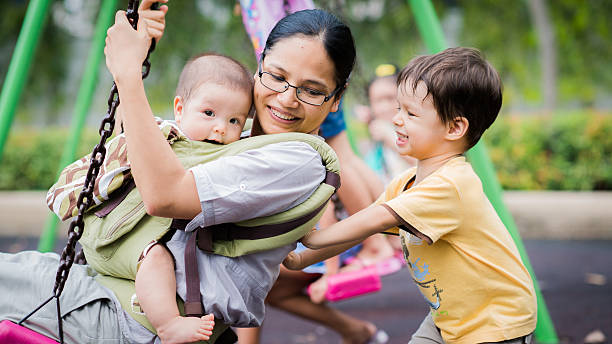 rapaz leva a sua mãe e bebé irmão em um balanço - child jungle gym playground laughing imagens e fotografias de stock