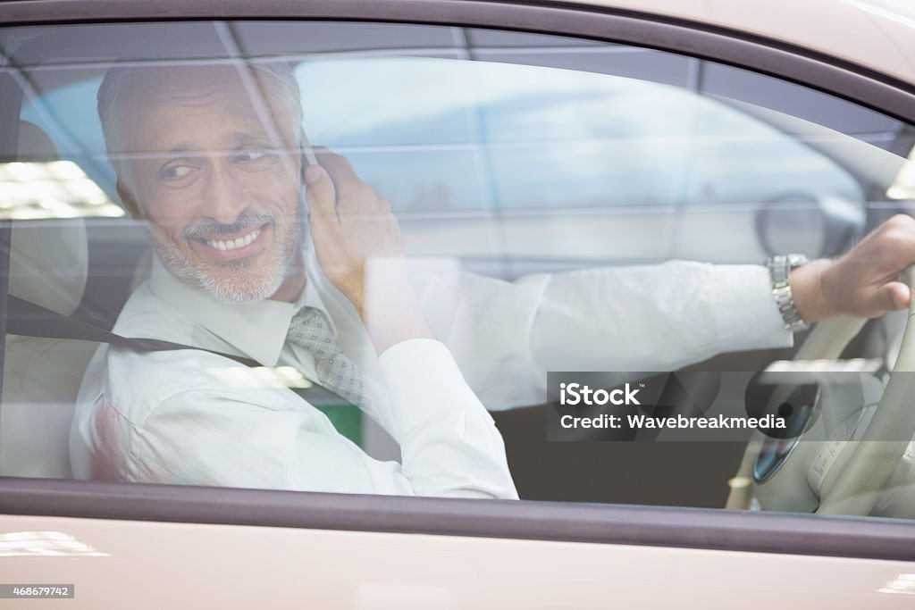 Smiling businessman on the phone in his car Smiling businessman on the phone in his car at new car showroom 2015 Stock Photo