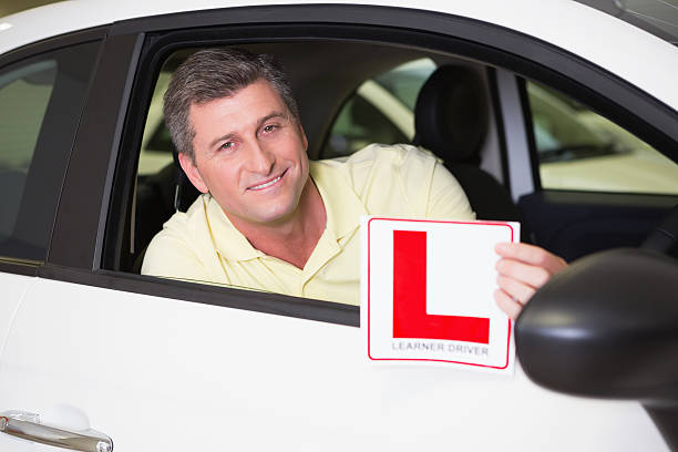 istock Man holding a learner driver sign sitting behind the wheel 468680730