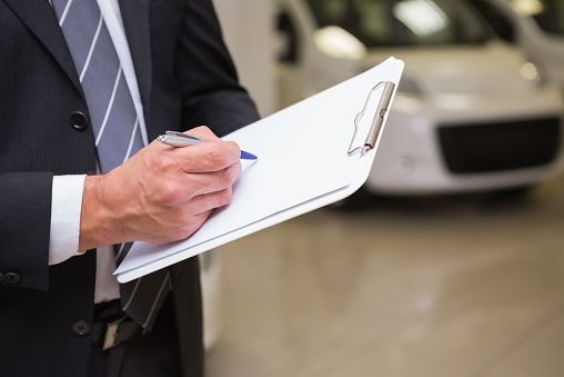 Close up of businessman writing on clipboard at new car showroom