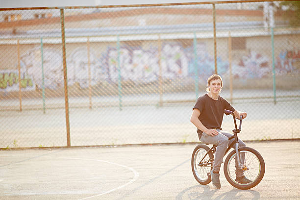 Smiling teenage boy sitting on his BMX bike and listening to music with earphones