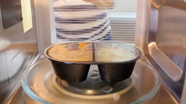 Woman Putting TV Dinner Into Microwave Oven To Cook